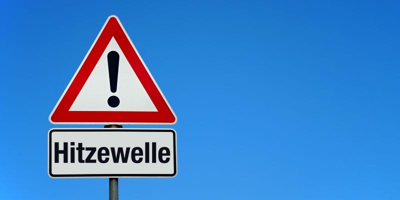 Gefahrenschild mit Zusatztafel "Hitzewelle" vor blauem Himmel