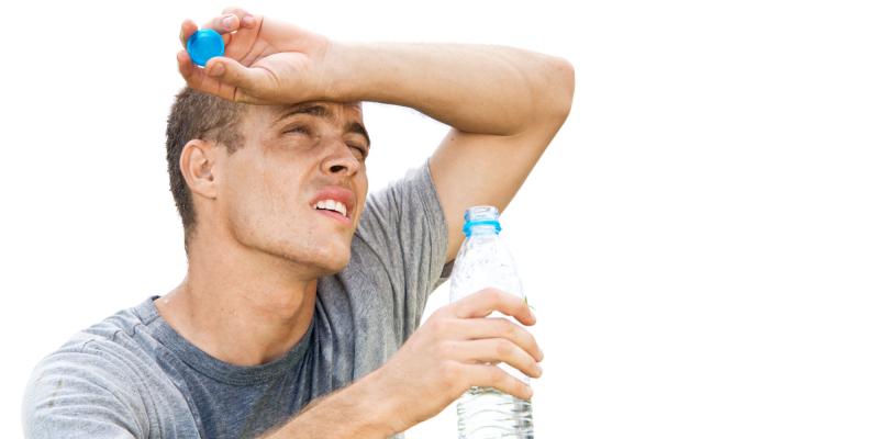 junger Mann mit Wasserflasche in der einen Hand, die andere auf der Stirn