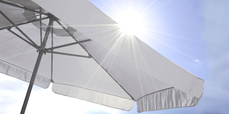 heller Sonnenschirm vor blauem Himmel mit Sonne