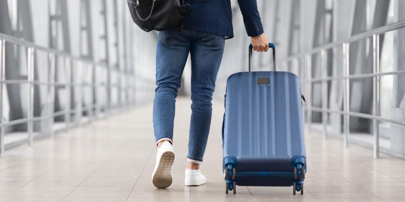 Mann zieht in Flughafengebäude blauen Hartschalenrollkoffer