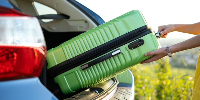 grüner Hartschalenkoffer wird in Autokofferraum gewuchtet
