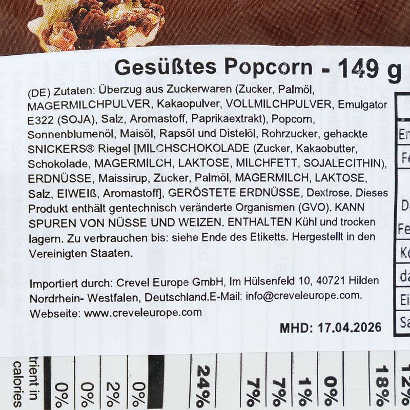 „Gesüßtes Popcorn", 149 Gramm: deutsche Zutatenliste mit Zuckerwaren-Überzug, gehackten „Snickers"-Riegeln und gerösteten Erdnüssen. Hinweise: enthält gentechnisch veränderte Organismen, kann Spuren von Nüssen und Weizen enthalten. Importiert durch Crevel Europe GmbH, hergestellt in den USA. Mindestens haltbar bis 17.04.2026.