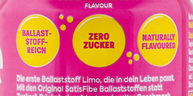 Verpackungsausschnitt mit drei Auslobungen in gelben Kreisen: „Ballaststoffreich“, „Zero Zucker“ und „Naturally flavoured“. Darunter der Werbeslogan „Die erste Ballaststoff Limo, die in dein Leben passt“.