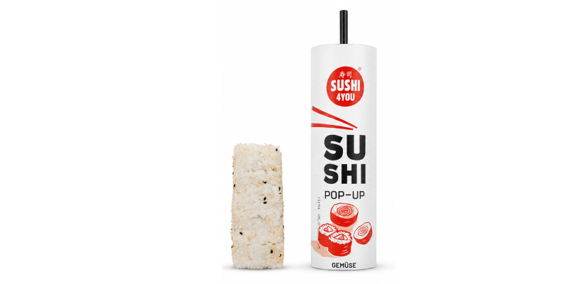 „Sushi Pop-Up" „Gemüse" von „Sushi 4You": aus der weißen Tube ist ein zylindrischer Reisblock mit Sesam herausgeschoben, oben ragt der schwarze Schiebestab heraus.