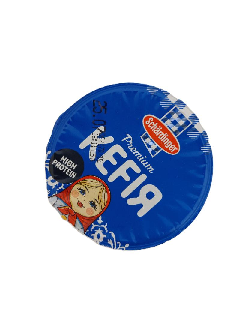 „Blauer Deckel eines Schärdinger Premium Kefir-Bechers mit High-Protein-Kennzeichnung und Matroschka-Motiv.“