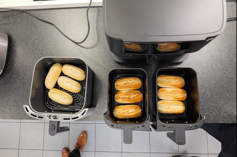 Aufsicht auf mehrere Heißluftfritteusen-Körbe mit aufgebackenen Weckerln, links vier hellere, rechts in zwei Schubladen je drei stärker gebräunte.